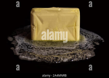 Ein Würfel mit Butter schmelzen auf einer schwarzen Platte auf schwarzem Hintergrund isoliert. Stockfoto