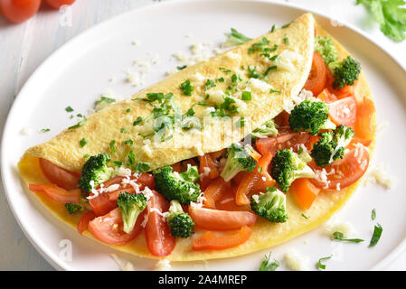 Nahaufnahme von gefülltes Omelett mit Tomaten, rote Paprika und Brokkoli auf hellem Holztisch. Gesunde Ernährung Essen zum Frühstück. Lecker morgen essen. Stockfoto