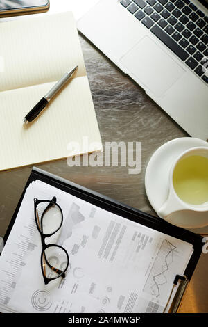 Hohe Betrachtungswinkel von Dokumenten mit finanzcharts Tasse Tee und Laptop auf dem Tisch befindet. Stockfoto