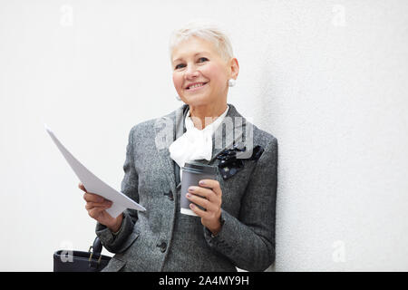 Portrait von erfolgreichen reife Geschäftsfrau holding Vertrag und Tasse Kaffee und lächelnd in die Kamera im Freien Stockfoto