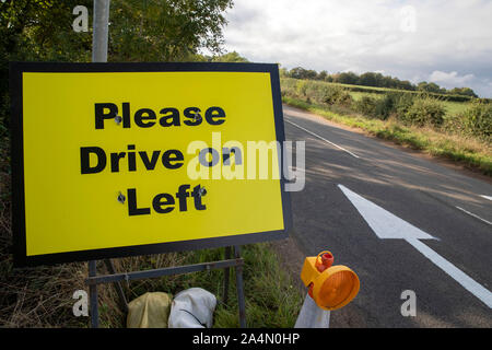 Bitte fahren Sie auf der linken Seite Schilder und Pfeile auf die B4031 Straße RAF Croughton, in Northamptonshire, wo Harry Dunn, 19, starb, als sein Motorrad in einem Kopf beteiligt war gelegt - auf Kollision im August. Stockfoto