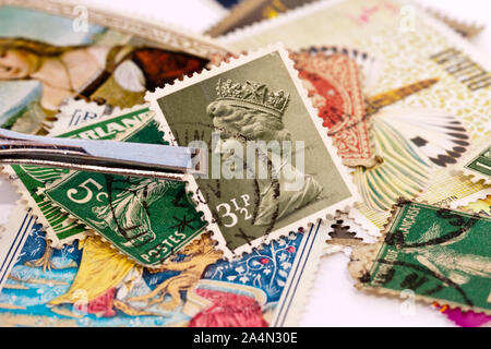 Pinzette Holding ein britischer Briefmarke mit Queen Elizabeth 2 Seite portrait. Sammlungen von Briefmarken im Hintergrund. Stockfoto