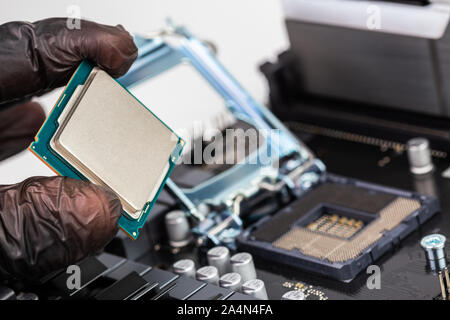 Hand in Kunststoff schwarz Handschuh holding Central Processor Unit vor der Installation auf blurry geöffnet Sockel auf dem Mainboard Hintergrund Stockfoto