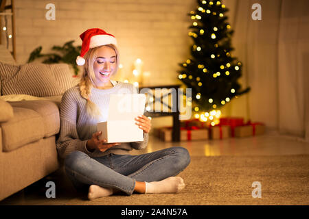 Der Weihnachtszeit. Glückliches Mädchen mit weihnachtsmütze Eröffnung Geschenkbox Stockfoto