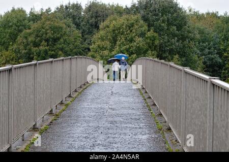 Rückansicht eines älteren Paares mit Regenschirm gehen über eine Fußgängerbrücke im Regen, Shepperton Surrey England Großbritannien Stockfoto