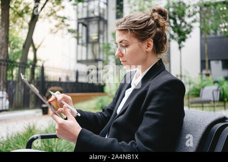 Portrait junge geschäftsfrau im Cafe sitzen auf der Veranda und mit einem digitalen Tablet. Nachdenkliche Frau Brille mit Tablet für Notizen Stockfoto
