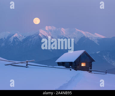 Weihnachten Landschaft mit einem verschneiten Haus in den Bergen. Märchen Nacht mit Vollmond. Winterlandschaft mit Spuren im Schnee. Stockfoto