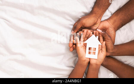 Schwarze Familie von drei Holding Papier Haus Abbildung in den Händen Stockfoto