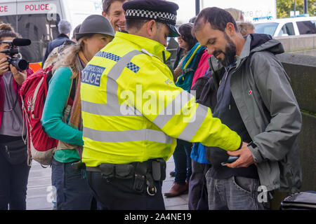 London, Großbritannien. 15. Oktober 2019. Ein Offizier sucht einen Mann. Obwohl die Met Polizei irgendwelche XR Proteste in Greater London unter Abschnitt 14 der öffentlichen Ordnung von 1986 verboten hatte, die Leute kamen noch außerhalb des MI5 o 9 n Millbank über vorhergesagte Zukunft Nahrungsmittelknappheit zu protestieren. Polizei durchsucht Aktivisten und bildete ein Anhalten, wenn ein Mann sich auf die Straße setzte. Aktivisten waren noch ankommen, wie ich es verlassen hatte. Peter Marshall / alamy Leben Nachrichten Stockfoto