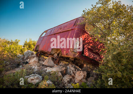 Abgebrochene van Bus auf den Felsen in der Mitte von Nirgendwo an einem sonnigen Tag. Unscharf Bäume im Vordergrund, Bild der Rückseite des Van. Stockfoto