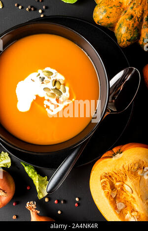 Kürbis creme Suppe mit Milch und Kürbiskerne in einem schwarzen Schüssel auf dem schwarzen Hintergrund. Close-up. Stockfoto