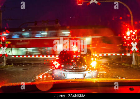 Ein Auto wartet vor einer geschlossenen Bahn Barriere während ein Zug vorbeifährt, Regen, Wetter, Dunkelheit, Stockfoto