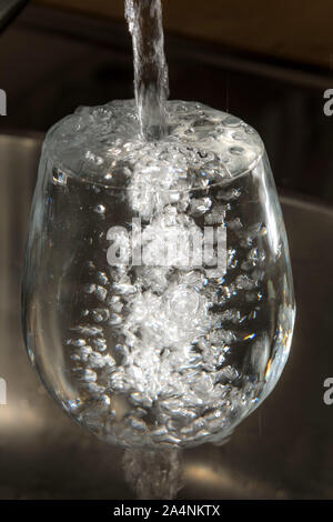 Fließt das Wasser aus einem Hahn in ein Glas. Symbol: Wasserverbrauch, Verschwendung von Wasser. Stockfoto