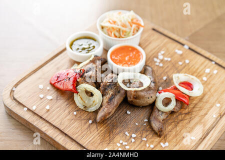 Lamm Zunge Kebab mit Sauerkraut und zwei Saucen. Serviert auf einem Holzbrett. Grill Restaurant Menü, eine Reihe von Fotos von verschiedenen Fleischsorten. Stockfoto