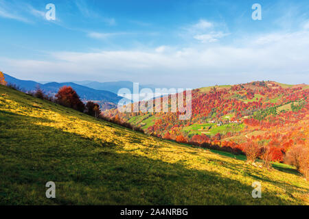 Schönen bergigen Landschaft bei Sonnenaufgang. Bäume in Rot Laub. wunderschöne Landschaft der Karpaten Landschaft. sonnigen Morgen Wetter mit Wolken Stockfoto