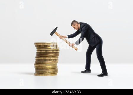 Seitenansicht des Geschäftsmannes Absturz großen goldenen Münzen mit Hammer stack, auf weißem Hintergrund Stockfoto