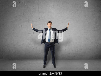 Junge Unternehmer steht Drücken unsichtbare Wände mit seinen Händen auf einen konkreten Hintergrund Stockfoto