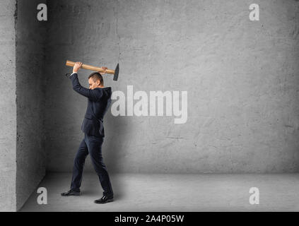 Seitenansicht eines Geschäftsmannes absturz Betonwand mit Hammer Stockfoto