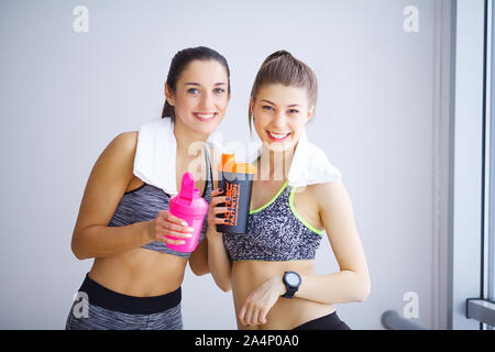 Porträt von zwei sportliche junge Damen mit Wasserflaschen und Handtuch in der Turnhalle posieren. Stockfoto