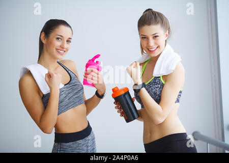 Porträt von zwei sportliche junge Damen mit Wasserflaschen und Handtuch in der Turnhalle posieren. Stockfoto