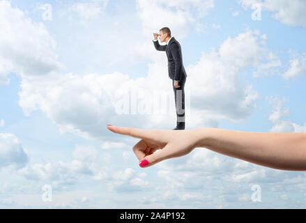 Unternehmer im Profil geradeaus schauen steht auf riesigen weiblichen Hand zeigt in die gleiche Richtung Stockfoto