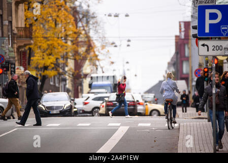 RIGA, Lettland. 15. Oktober, 2019. Dame auf dem Fahrrad wartet an Kreuzung zum grünen Licht, während die Fußgänger die Straße überqueren. Autos bewegen sich auf Ba Stockfoto