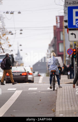 RIGA, Lettland. 15. Oktober, 2019. Dame auf dem Fahrrad wartet an Kreuzung zum grünen Licht, während die Fußgänger die Straße überqueren. Autos bewegen sich auf Ba Stockfoto