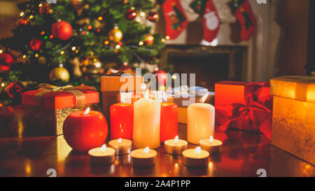 Schöne getonten Bild der brennenden Kerzen und Geschenke von Santa gegen glühende geschmückten Weihnachtsbaum und Kamin in der Nacht Stockfoto