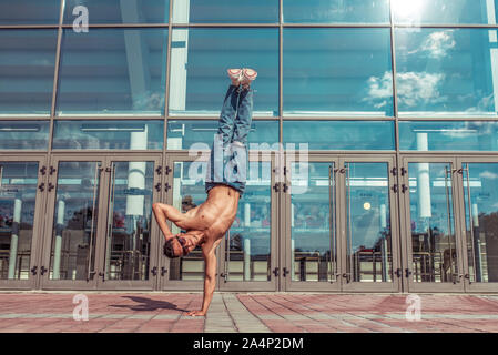 Tänzerin in Springe steht auf einem Arm, Acrobat Schauspieler Break Dance, Hip-hop. Im Sommer Stadt, Hintergrund Glasfenster wolken Lifestyle, junge Tänzerin, Fitness Stockfoto