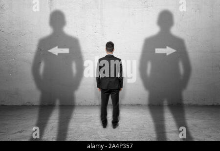 Geschäftsmann stand vor einer Betonwand mit Pfeilen, die in verschiedene Richtungen. Stockfoto