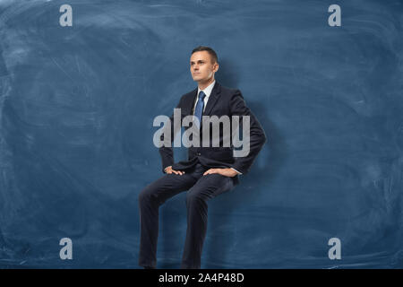Geschäftsmann sitzt und Denken auf blaue Tafel Hintergrund isoliert Stockfoto