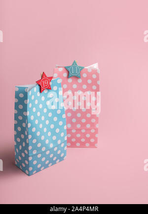 Weihnachten Adventskalender Konzept. Rosa und Blau Geschenkbeutel mit Zahlen auf einem rosa Hintergrund. Seine und ihre Geschenke. Bunte Geschenkbeutel. Stockfoto