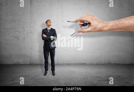 Kleine Geschäftsmann auf konkreten Hintergrund durch riesige Hand mit Metall Kompass gemessen wird. Stockfoto