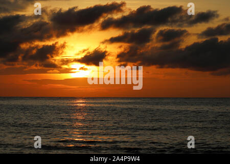 Sonnenuntergang über dem Meer, orange Sun in schwarz Wasser wider. Bunte dramatische Himmel mit dunklen Wolken, romantischen Hintergrund für Reisen und Urlaub Stockfoto