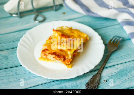 Portion leckere Lasagne auf weißem Teller auf blauem Holz Tabelle Stockfoto