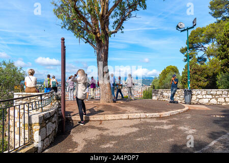 Touristen versammeln sich auf einem Aussichtspunkt Castle Hill in Nizza Frankreich, mit Blick auf das Meer und die Altstadt Vieux Nice als Musiker für Geld spielt. Stockfoto