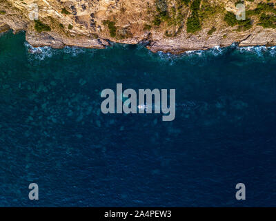 Luftaufnahme von einem steilen Felsen und ein Motorboot. Zerklüftete Küste an der Adria. Klippen mit Blick auf den transparenten Meer. Wilde Natur und Mittelmeer Stockfoto