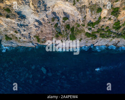 Luftaufnahme von einem steilen Felsen und ein Motorboot. Zerklüftete Küste an der Adria. Klippen mit Blick auf den transparenten Meer. Wilde Natur und Mittelmeer Stockfoto