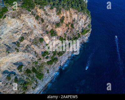 Luftaufnahme von einem steilen Felsen und ein Motorboot. Zerklüftete Küste an der Adria. Klippen mit Blick auf den transparenten Meer. Wilde Natur und Mittelmeer Stockfoto
