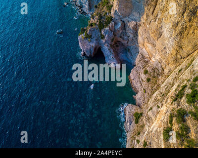 Luftaufnahme von einem steilen Felsen und ein Motorboot. Zerklüftete Küste an der Adria. Klippen mit Blick auf den transparenten Meer. Wilde Natur und Mittelmeer Stockfoto