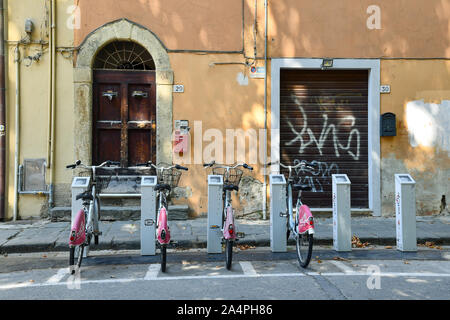 Zeile der öffentlichen Fahrräder, die zu einem Bike Sharing Station vor einem alten Gebäude im historischen Zentrum der berühmten Stadt Pisa, Toskana, Italien geparkt Stockfoto