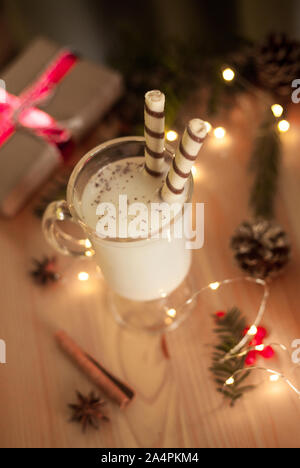 Traditionelle weihnachtliche Getränk Eierlikör mit Süßigkeiten und Gewürzen. Ansicht von oben. Selektive konzentrieren. Verschwommen Lichterketten. Stockfoto