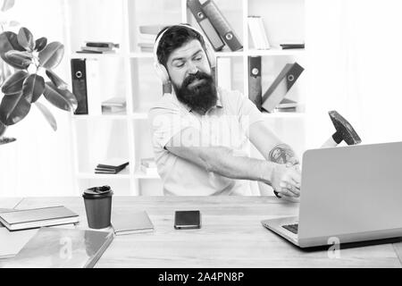 Computer lag. Gründe für Computer zurückbleiben. Wie fix langsam hinterher. Hasse office Routine. Man bärtige Kerl Kopfhörer Büro schwingen Hammer auf dem Computer. Langsame Internetverbindung. Veraltete Software. Stockfoto