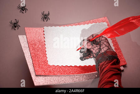 Kreative lila und rosa Halloween mockup mit Hand in Schwarz mesh Handschuh Holding leuchtend rote Feder, mit mehr Papier und einige Spinnen Stockfoto