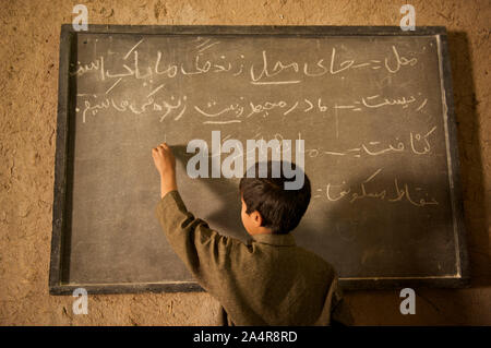 Ein Student schreibt auf eine Tafel, an der Gemeinschaft gegründete Schule (CBS) in einer Moschee, in Qala-e-Haji Yahya Dorf, in Anjil Bezirk der Provinz Herat, Afghanistan. Insgesamt 395 Kinder besuchen diese Gemeinschaft informellen Grundschule in drei Klassen von Klasse 1 bis Klasse 3. Es gibt fünf Lehrer für die drei Klassen. Afghanistan. 7. Mai 2009 Stockfoto