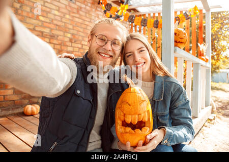 Halloween Einlieferung am Konzept. Junge Paare an der Veranda sitzen mit Jack-o'-Lantern unter selfie posiert für die Kamera glücklich Stockfoto