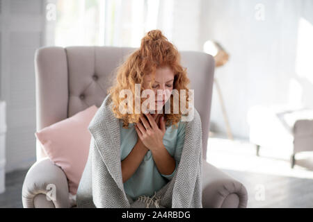 Frau Husten beim Sitzen auf einem Sessel in Krankheitsurlaub Stockfoto