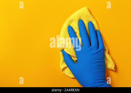 Eine Hand in einem schützenden latex Handschuh hält einen Lappen auf einem gelben Hintergrund. Stockfoto