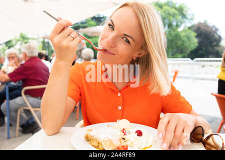 Junge Frau sitzt in einem Cafe in Wien und frisst Österreichs traditionelle süße Apfelstrudel mit Sahne und Vanilleeis, Wien, Österreich Stockfoto