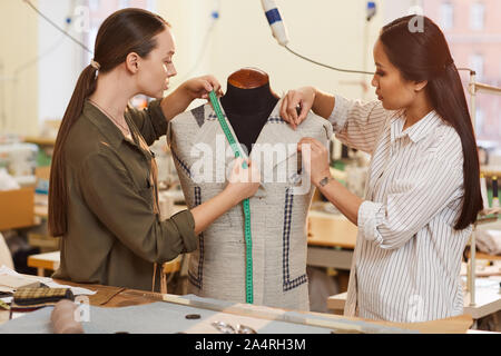 Zwei junge Modedesigner stehen in der Nähe der Puppe und Messungen mit Maßband zusammen in der Werkstatt Stockfoto